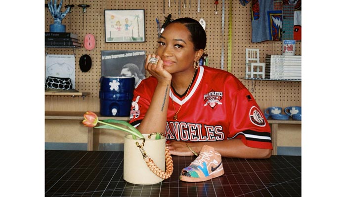 A woman sits at a table with a ceramic purse and sneaker on the table in front of her.