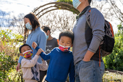 Two small children wearing face masks in the Getty Central Garden with their parents. 