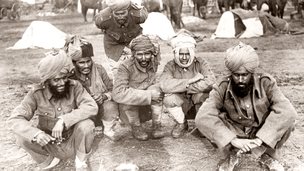 Black and white photo of men sitting on ground with head wraps.